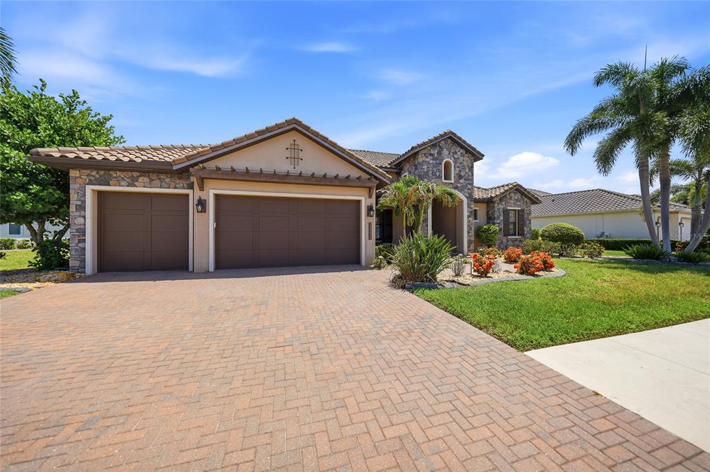 A single-story house with a stone facade, a brick paver driveway, and a three-car garage — 13220 CAMPANILE COURT, VENICE, FL