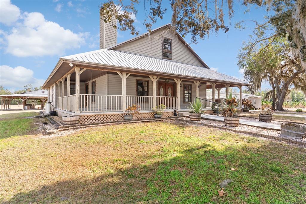 A two-story house with a metal roof and a wrap-around porch sits on grass — 17620 POYNER ROAD N, POLK CITY, FL