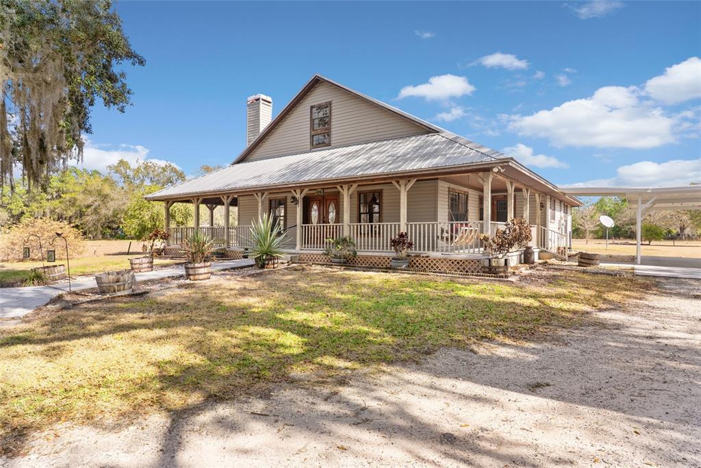 A tan house with a metal roof and a wrap-around porch sits on a lot — 17620 POYNER ROAD N, POLK CITY, FL