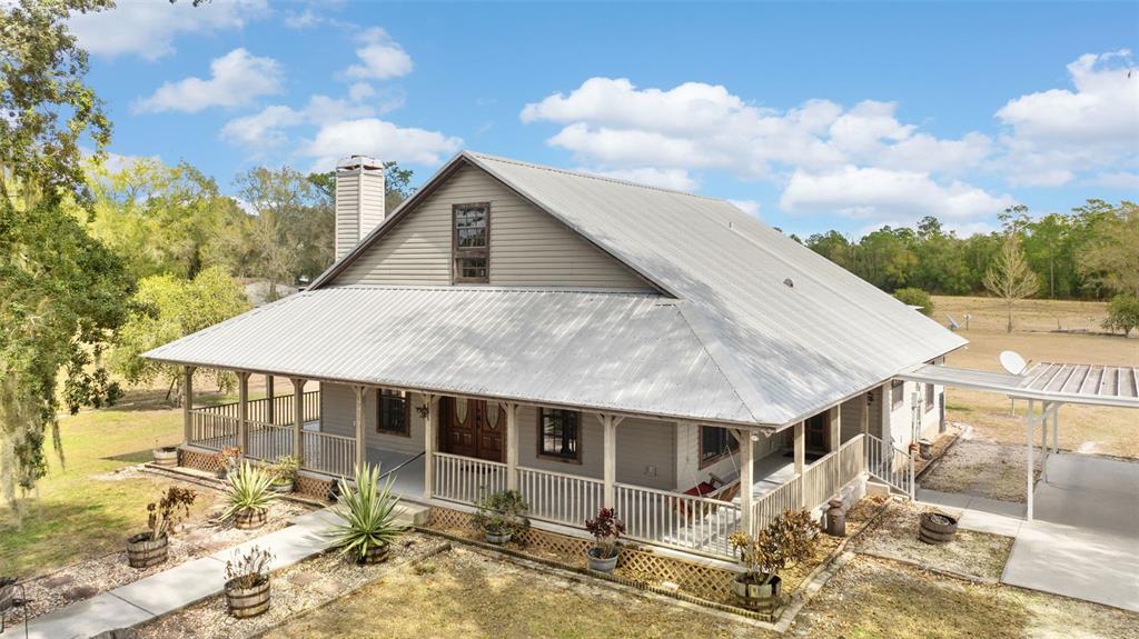 An elevated exterior view of a house with a metal roof and a wraparound porch — 17620 POYNER ROAD N, POLK CITY, FL