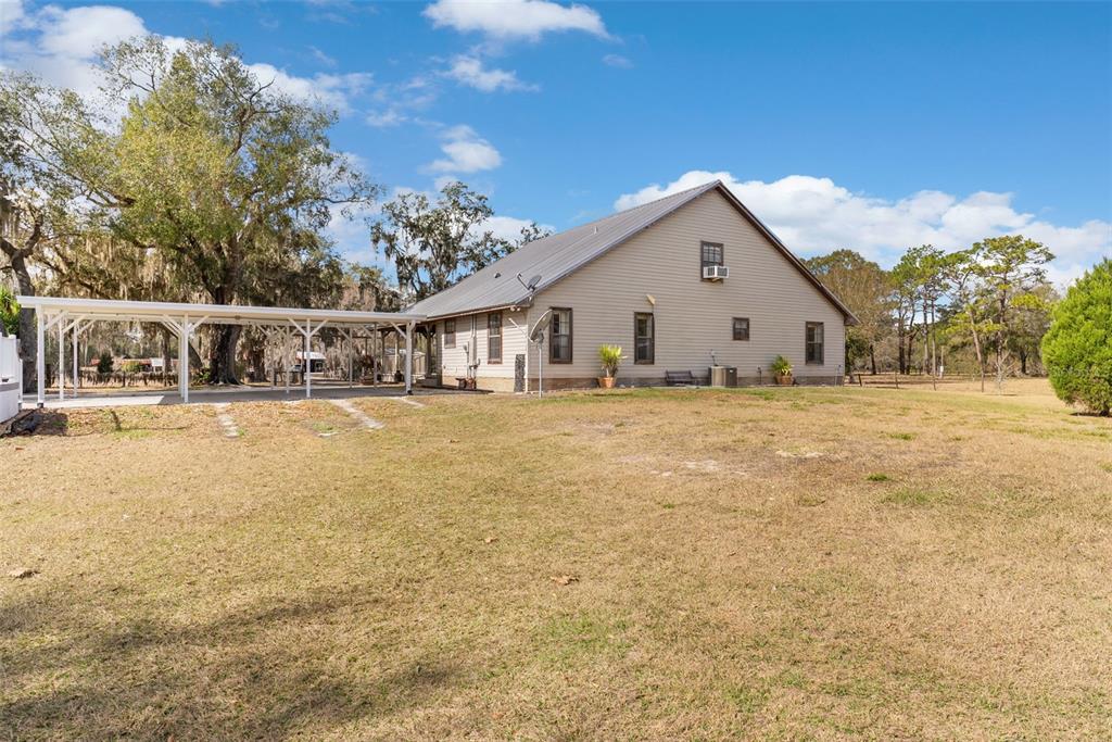 A tan house with a metal roof and an attached white carport sits on grass — 17620 POYNER ROAD N, POLK CITY, FL