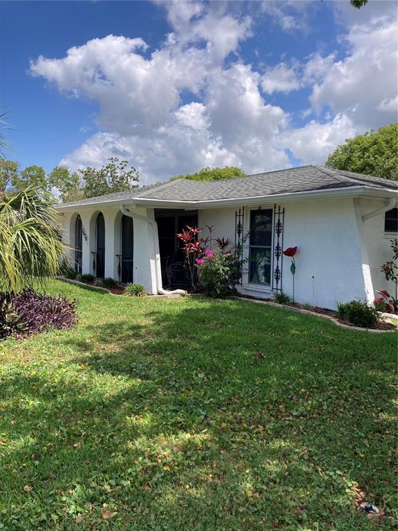 A white single-story house with arched windows and a shingled roof sits on a lawn — 7628 VALLEY COURT, NEW PORT RICHEY, FL