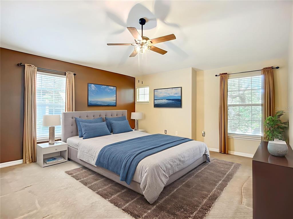 A bedroom features a gray upholstered bed, brown accent wall, and two windows with curtains — 6811 BREEZY PALM DRIVE, RIVERVIEW, FL