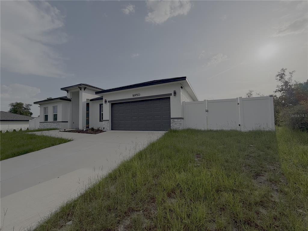 A modern single-story house with a white exterior, dark garage door, and white vinyl fence — 16950 SW 42ND AVENUE ROAD, OCALA, FL