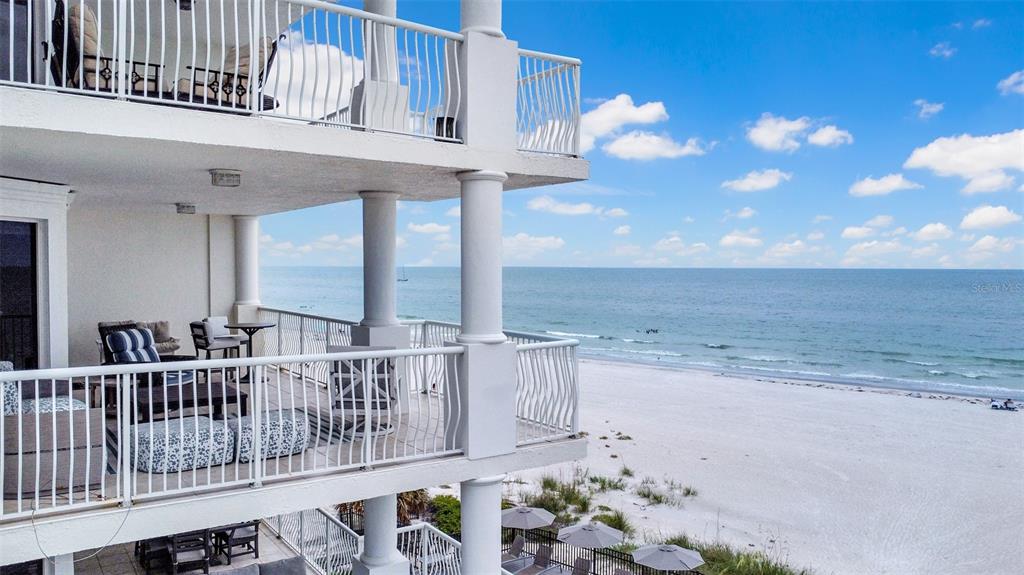A multi-story balcony overlooks a sandy beach and the ocean under a blue sky — 19734 GULF BOULEVARD UNIT 402, INDIAN SHORES, FL