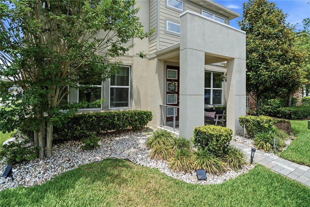 A modern home exterior features a concrete entryway, a dark front door, and landscaped gardens — 16185 TALIESIN STREET, WINTER GARDEN, FL