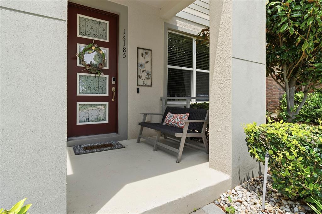 A front porch features a red door with glass panels, a bench, and a welcome mat — 16185 TALIESIN STREET, WINTER GARDEN, FL