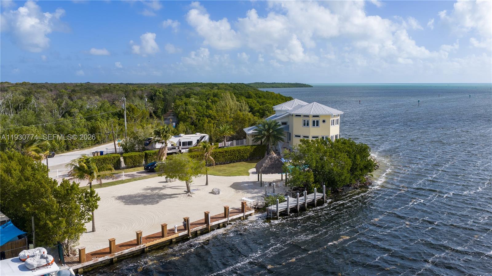 An aerial view shows a yellow house with a dock, sandy yard, and RV — 57 Garden Cove Dr, Key Largo FL 33037, KEY LARGO, FL