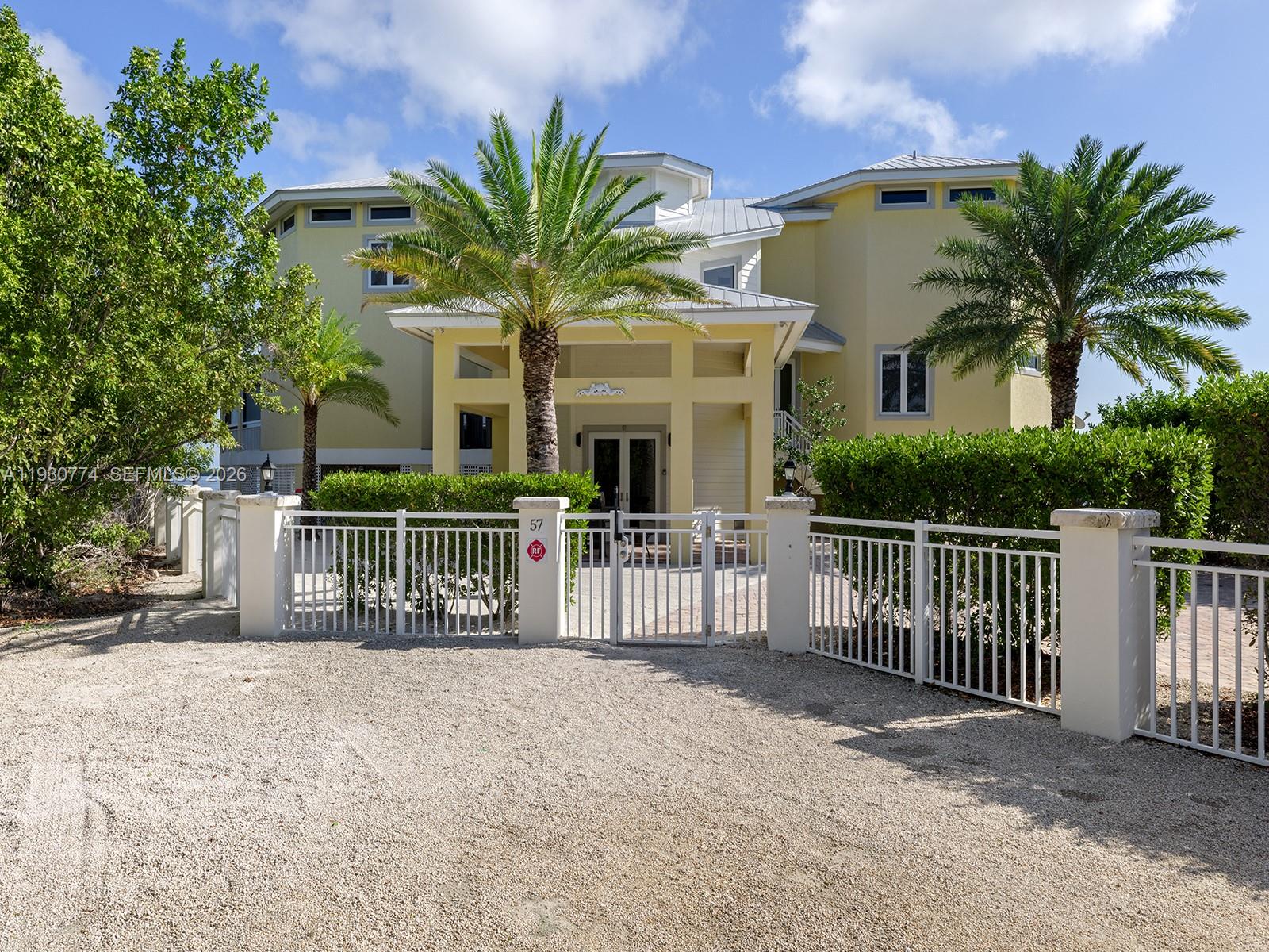 A yellow two-story house with a palm-lined entrance and a white metal fence — 57 Garden Cove Dr, Key Largo FL 33037, KEY LARGO, FL