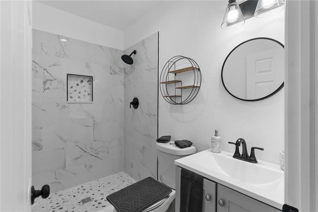 A bathroom features a walk-in shower with marble-look tile, a vanity, and a circular mirror — 412 E HARWOOD STREET UNIT 3, ORLANDO, FL