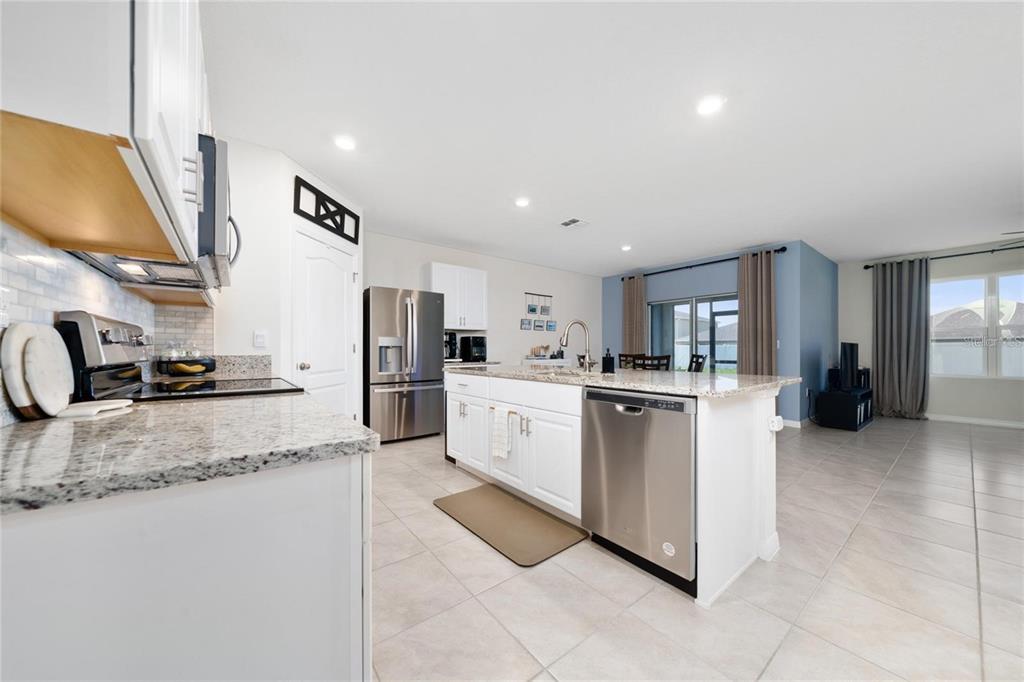 A kitchen with white cabinets, granite countertops, and stainless steel appliances opens to a living area — 1687 PARK SIDE AVENUE, KISSIMMEE, FL