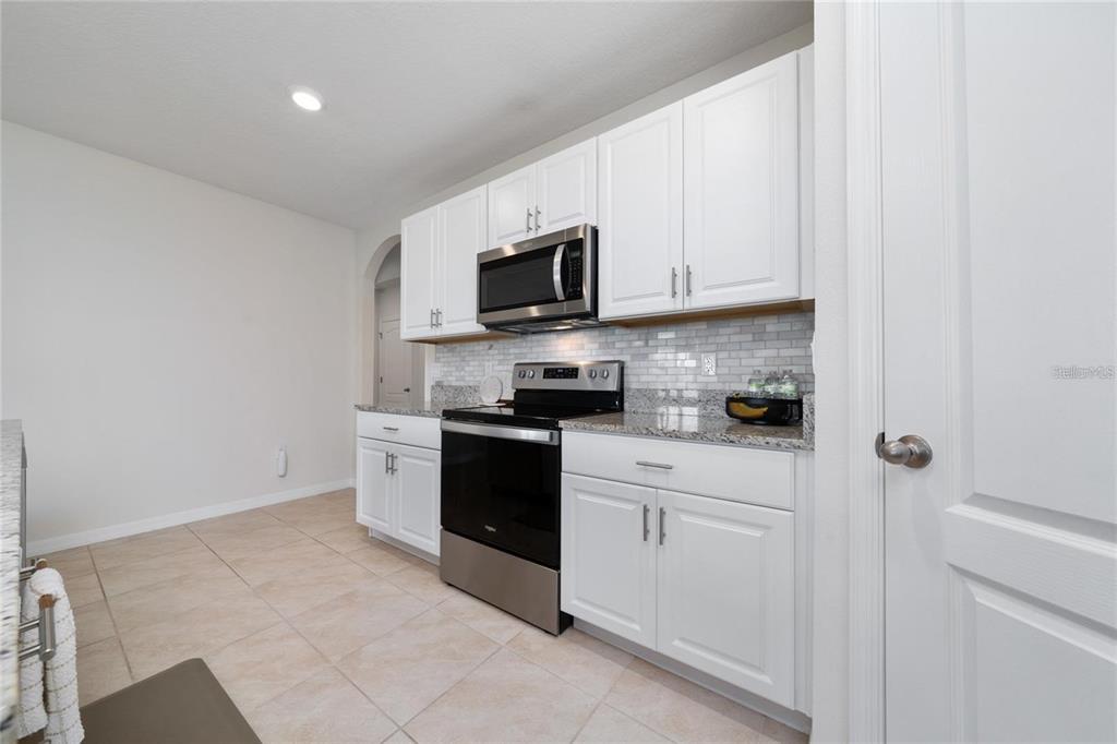 A kitchen features white cabinets, granite countertops, a subway tile backsplash, and stainless steel appliances — 1687 PARK SIDE AVENUE, KISSIMMEE, FL