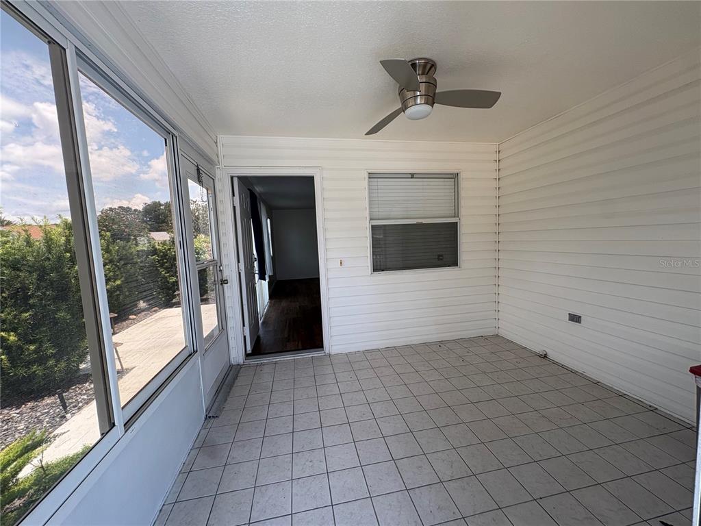 A tiled sunroom features a ceiling fan, white siding walls, and a door to the interior — 731 DUMAS STREET, THE VILLAGES, FL