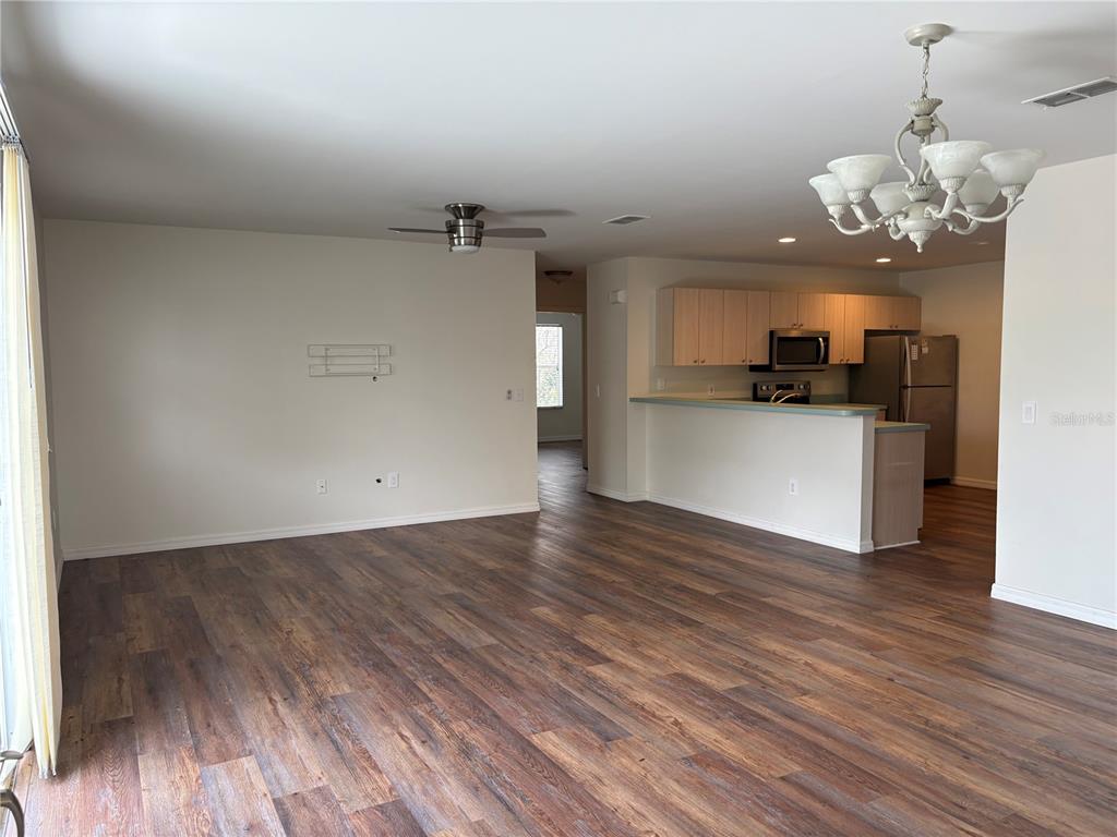 An open-concept living area features wood-look flooring, a ceiling fan, and an adjacent kitchen — 731 DUMAS STREET, THE VILLAGES, FL
