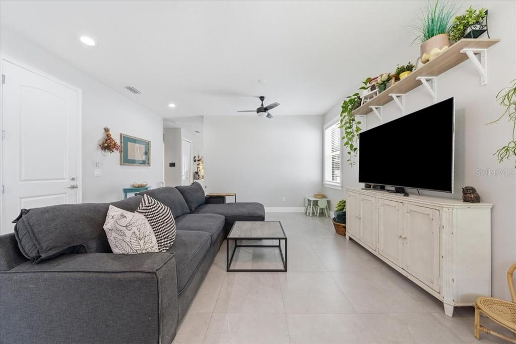 A living room features a grey sectional sofa, a television on a white cabinet, and shelving — 1808 W CLUSTER AVENUE, TAMPA, FL