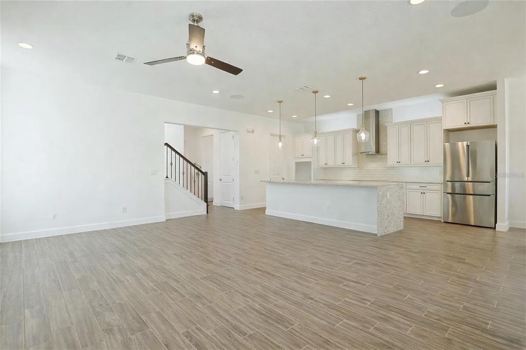 An open-concept kitchen and living area features light wood-look tile flooring and white cabinetry — 7038 ARNOLDSON STREET, ORLANDO, FL