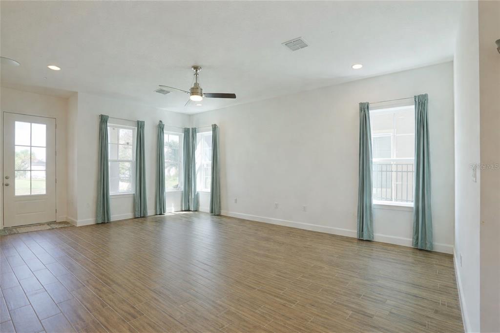 A spacious living room features light walls, wood-look tile flooring, and multiple windows with curtains — 7038 ARNOLDSON STREET, ORLANDO, FL