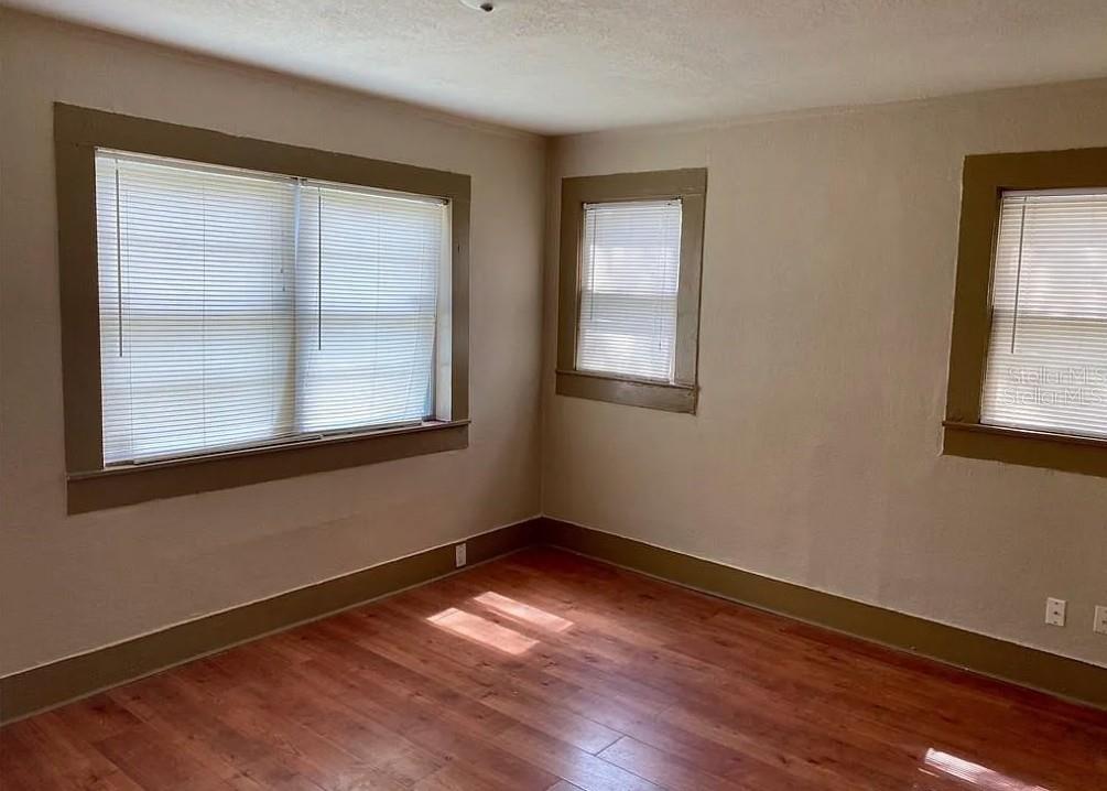 An empty room with wood-look flooring, beige walls, and three windows with white blinds — 110 W 13TH STREET, SANFORD, FL