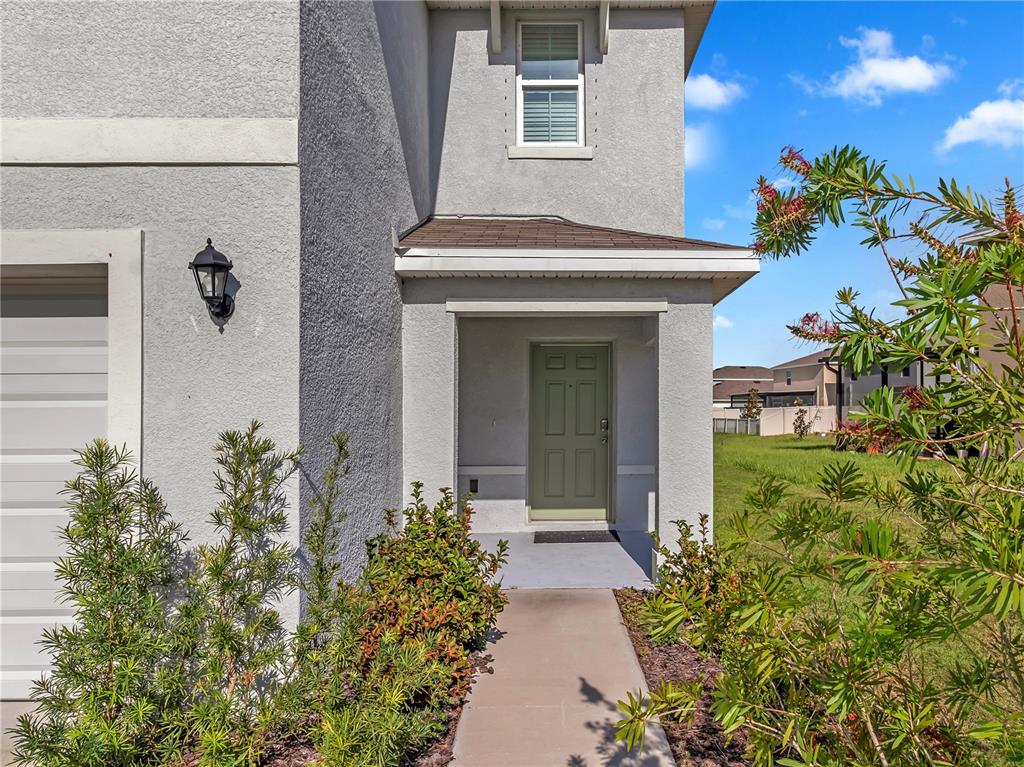 A gray stucco house exterior features a covered entryway with a light green front door — 16638 MOSAIC OAR DRIVE, WIMAUMA, FL