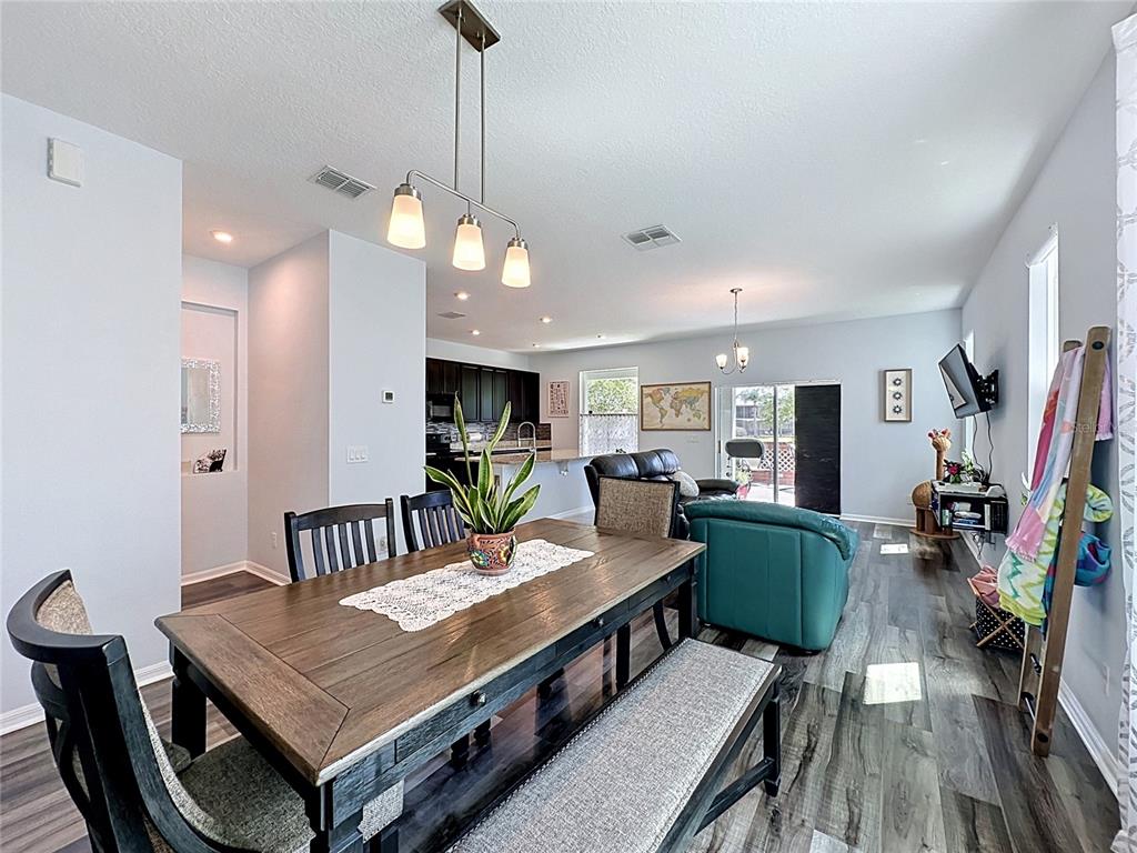 An open-concept dining and living area features a wooden table, dark flooring, and kitchen access — 246 ABERDEEN ST, DAVENPORT, FL