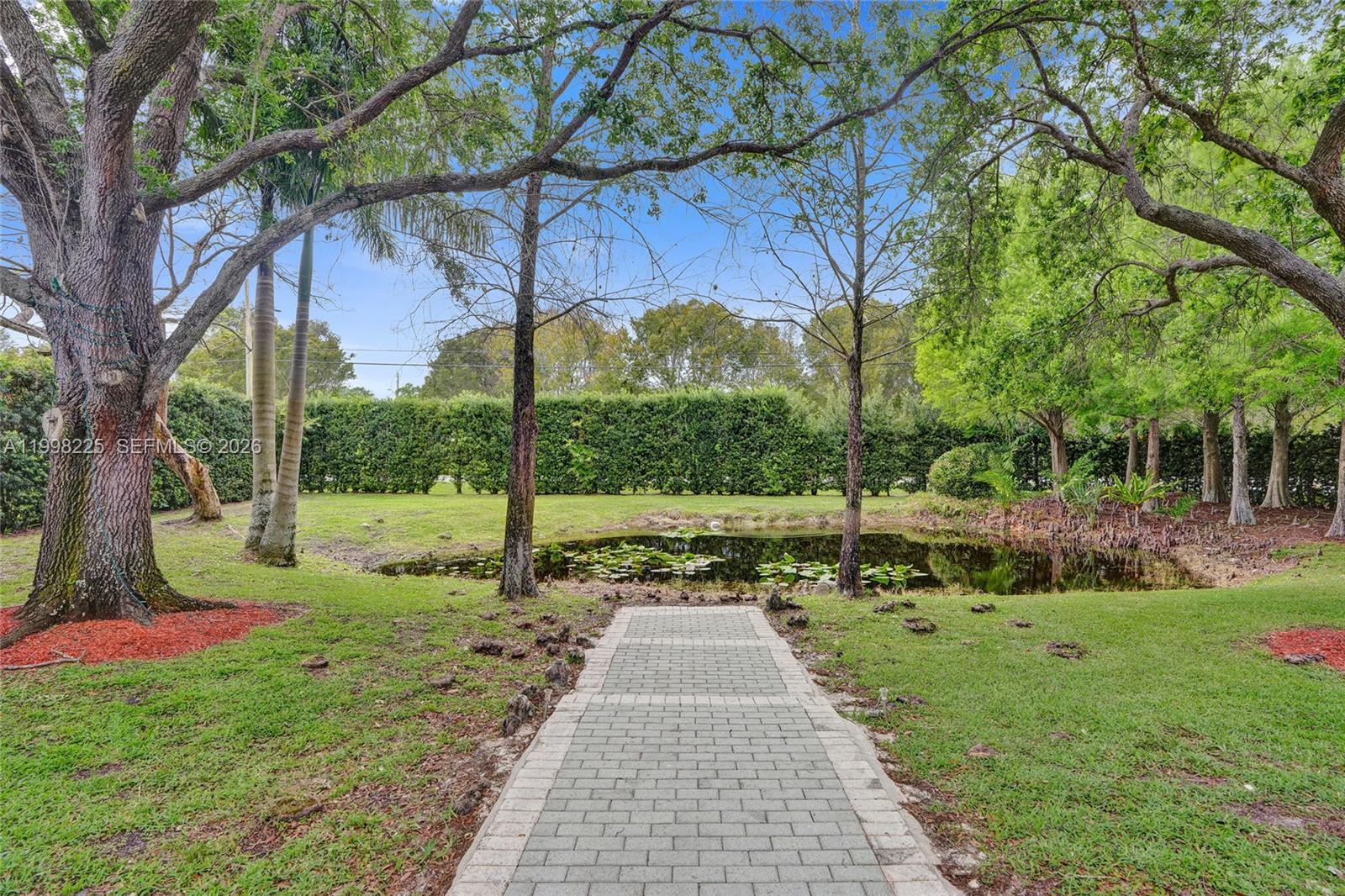 A paved walkway leads toward a small pond surrounded by trees and a hedge — 12350 NW 6th St, Plantation FL 33325, PLANTATION, FL