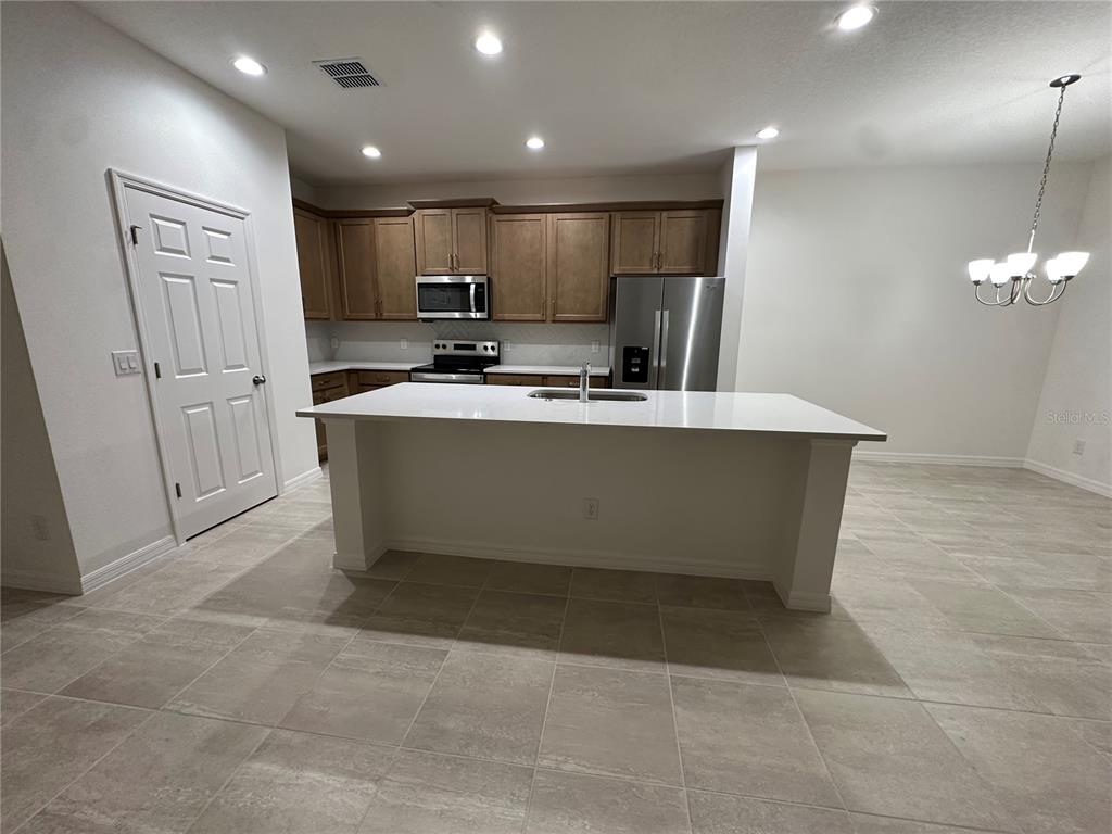 A kitchen features a white island, stainless steel appliances, and wood cabinets on tile flooring — 668 BIRDSWILL LANE, DELAND, FL