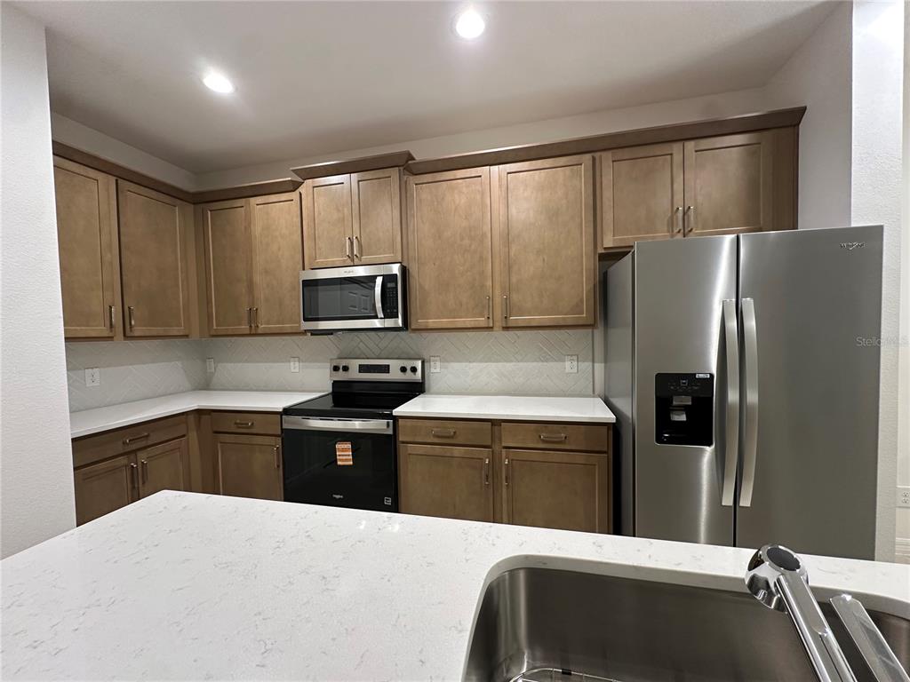 A kitchen features wood cabinets, stainless steel appliances, white countertops, and a herringbone tile backsplash — 668 BIRDSWILL LANE, DELAND, FL