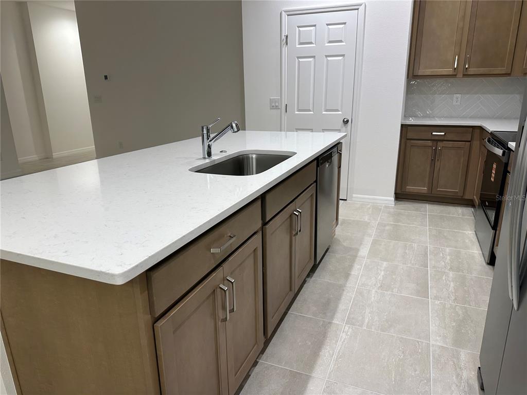 A kitchen island with a sink and white countertop sits before brown cabinets and tile — 668 BIRDSWILL LANE, DELAND, FL