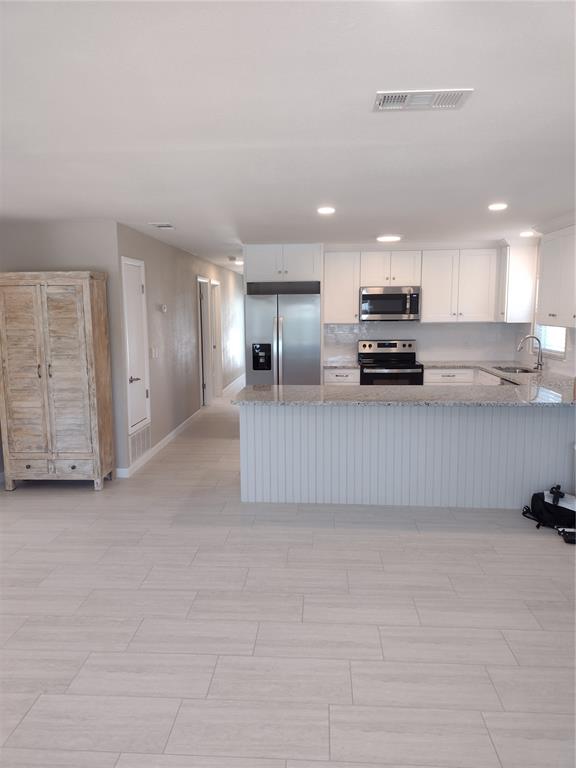 A kitchen with white cabinets, stainless steel appliances, and a peninsula overlooks a tiled room — 830 E 18TH AVENUE, NEW SMYRNA BEACH, FL