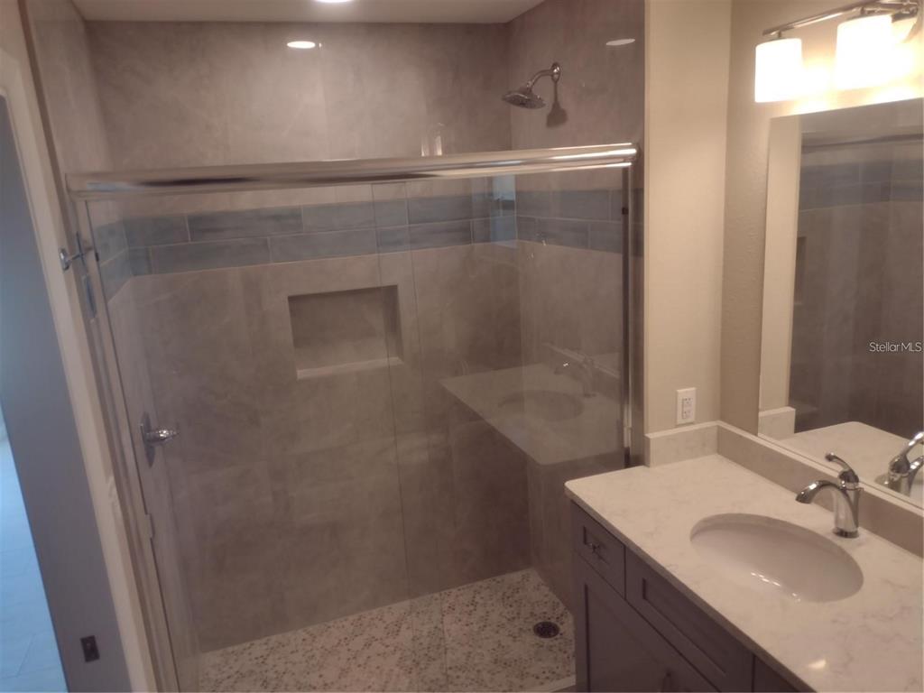 A bathroom features a glass-enclosed shower with tiled walls and a single-sink vanity — 830 E 18TH AVENUE, NEW SMYRNA BEACH, FL
