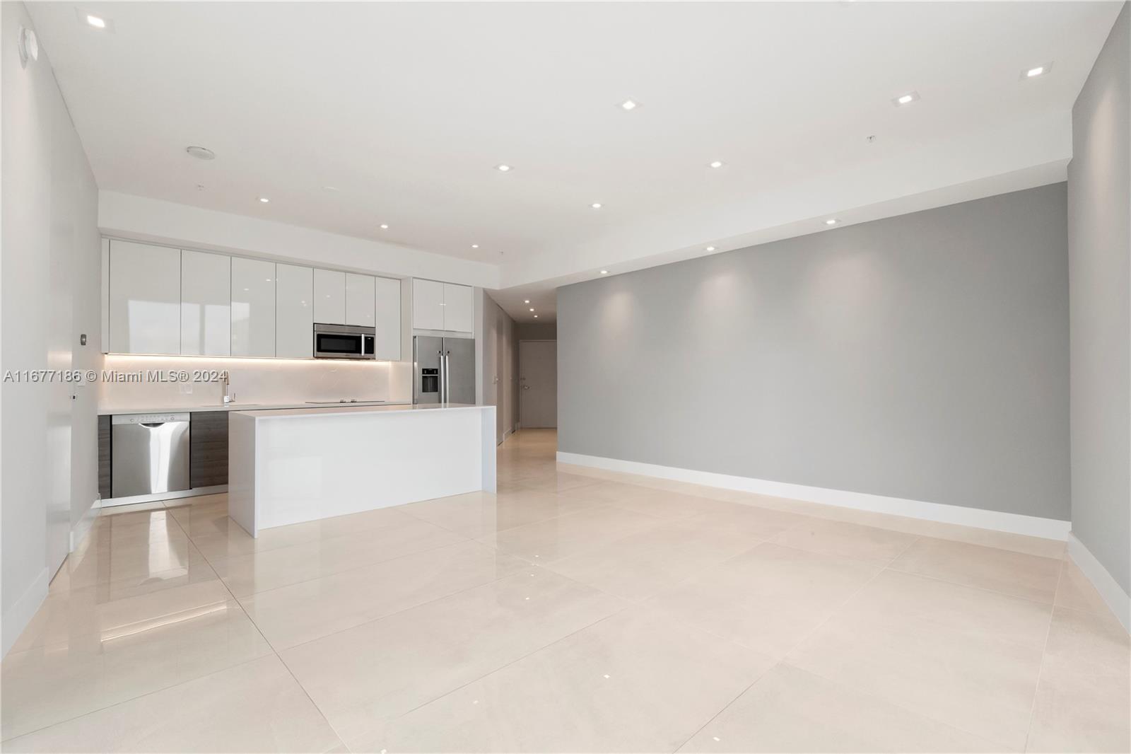A modern kitchen with white cabinetry and a central island opens into a spacious room — 1010 SW 2nd Ave, Miami FL 33130, MIAMI, FL