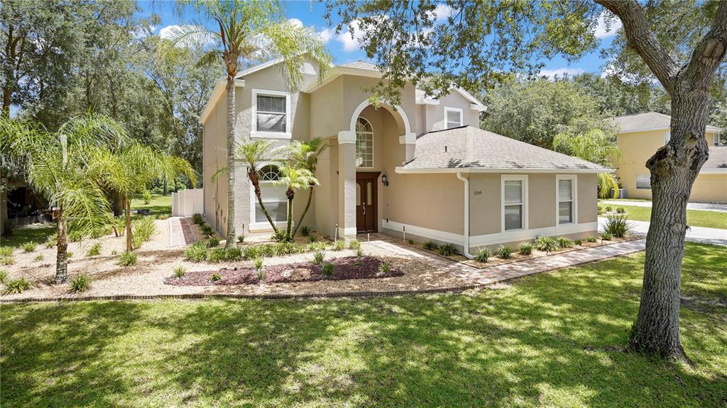 A two-story tan house with a arched entryway, palm trees, and a landscaped front yard — 1355 EDISON TREE ROAD, APOPKA, FL