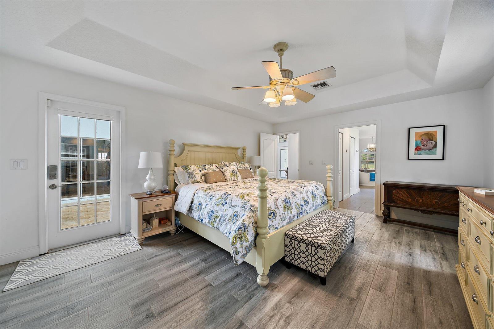 A bedroom features a four-poster bed, wood-look tile flooring, a ceiling fan, and a door — 13033 Randolph Siding Road N, Jupiter FL 33478, JUPITER, FL