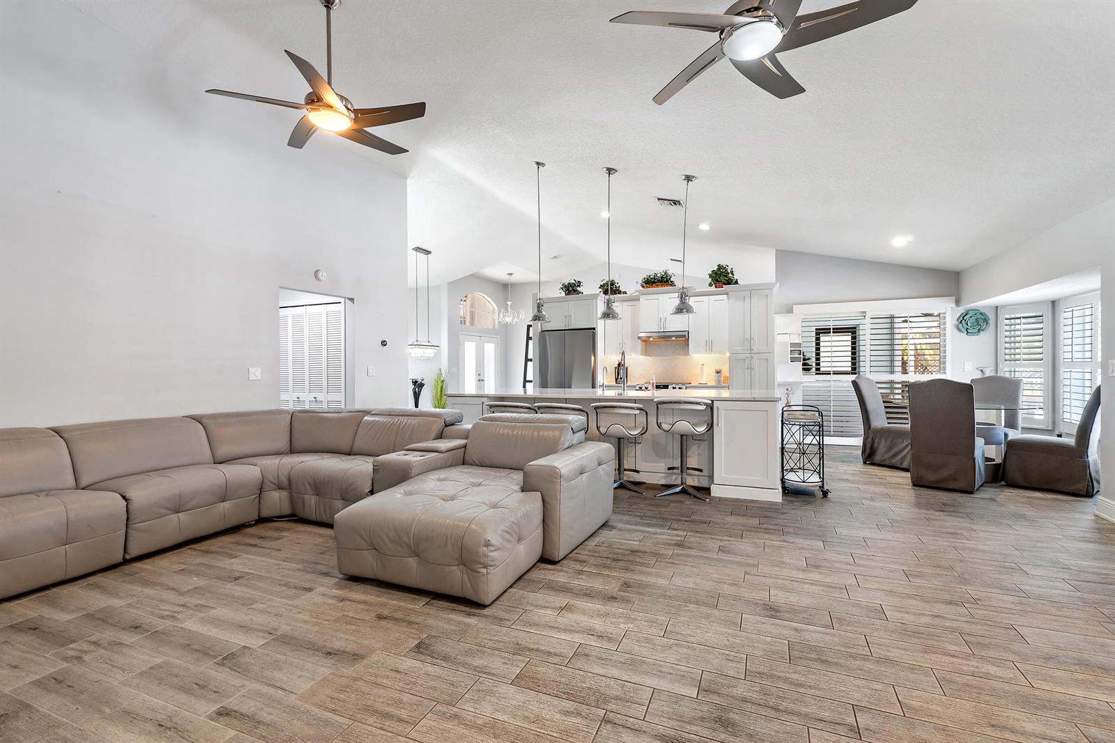 An open-concept living room and kitchen feature light-colored tile flooring and two ceiling fans — 13033 Randolph Siding Road N, Jupiter FL 33478, JUPITER, FL