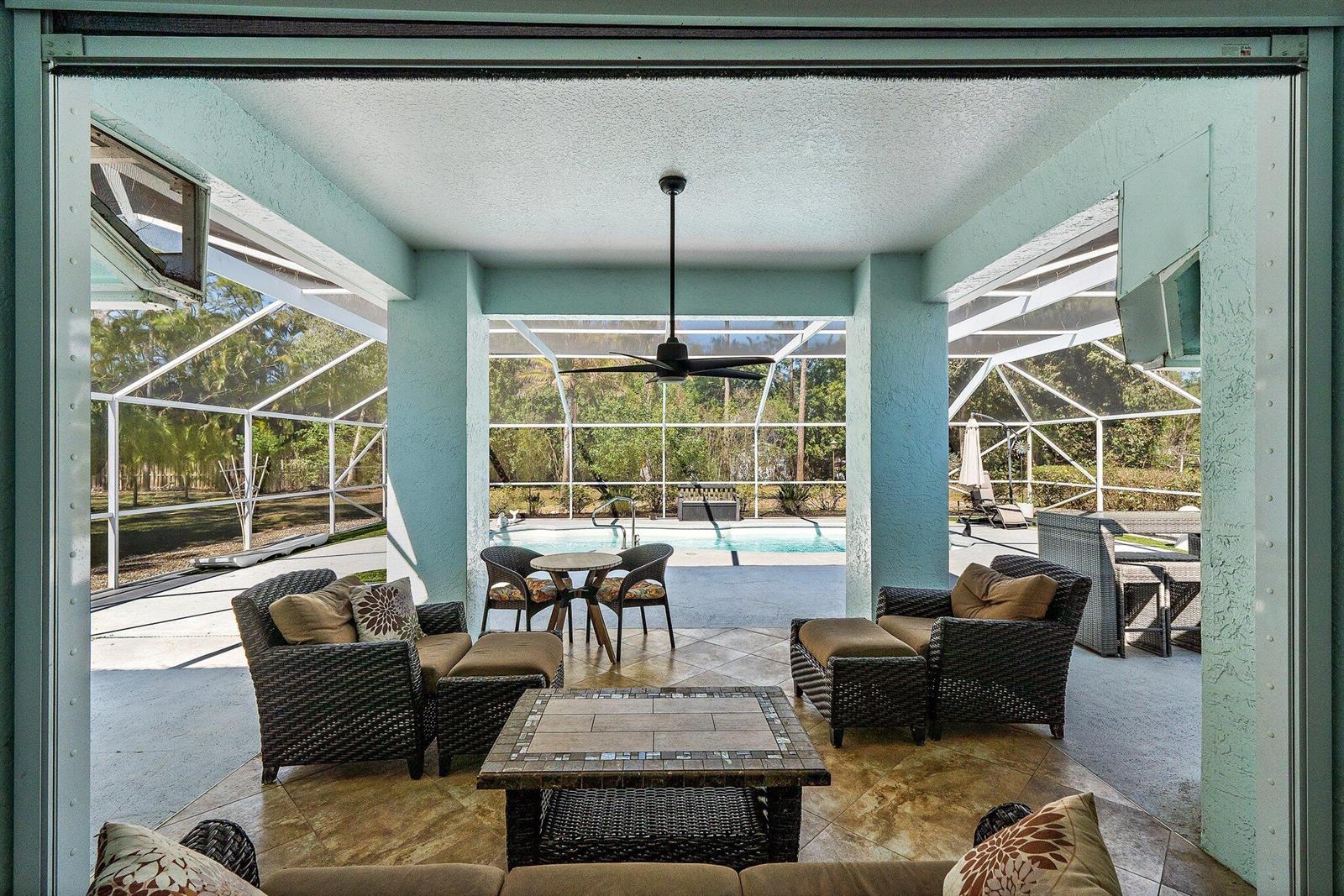 A covered patio features wicker furniture, a tiled floor, and a view of a screened pool — 13033 Randolph Siding Road N, Jupiter FL 33478, JUPITER, FL