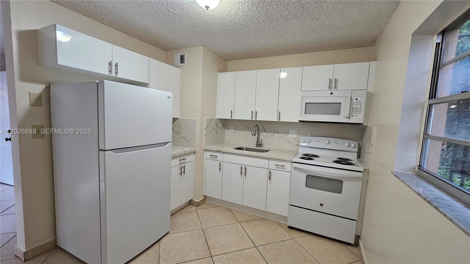A kitchen features white cabinets, stainless steel appliances, and light-colored countertops with a backsplash — 1235 NW 6th St # 3, Miami FL 33125, MIAMI, FL