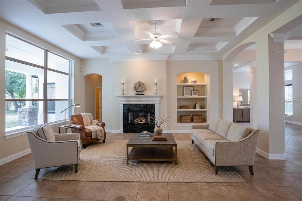 A living room features a fireplace, built-in shelving, a coffered ceiling, and tile flooring — 25609 HAWKS RUN LANE, SORRENTO, FL