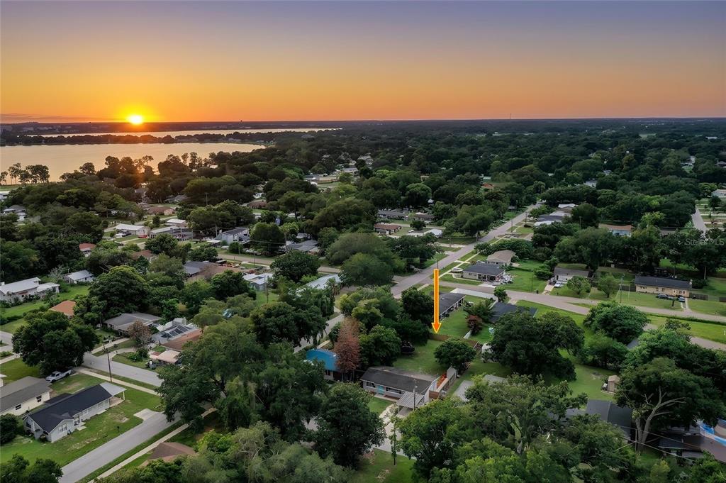 An aerial view shows a residential neighborhood at sunset with an orange arrow pointing toward a lot — 3004 AVENUE S NW, WINTER HAVEN, FL