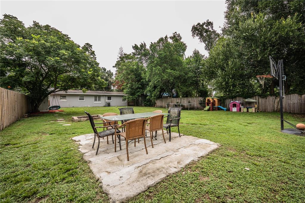 A backyard features a concrete patio with a dining set, a basketball hoop, and trees — 3004 AVENUE S NW, WINTER HAVEN, FL