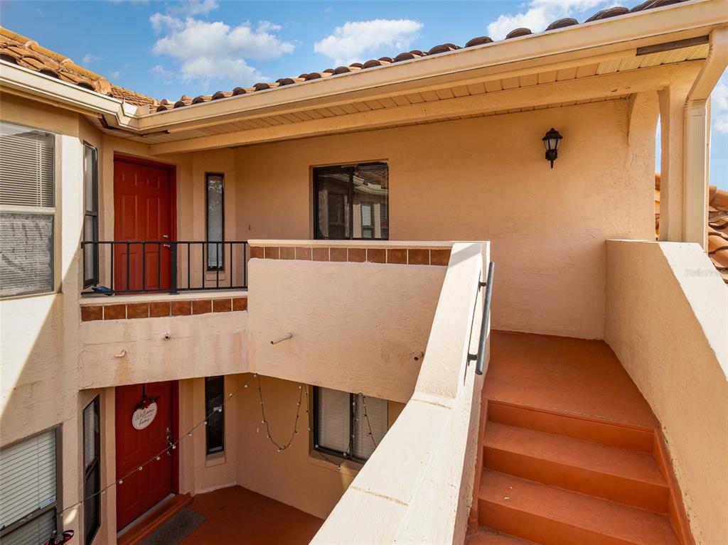 An exterior view of a two-story building with red doors, stairs, and a balcony — 7654 SUGAR BEND DR DRIVE UNIT 7654, ORLANDO, FL