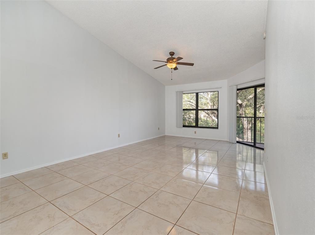 An empty living room features vaulted ceilings, light-colored tile flooring, a ceiling fan, and windows — 7654 SUGAR BEND DR DRIVE UNIT 7654, ORLANDO, FL