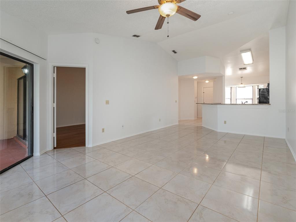 A bright, open-concept living area features white walls, tiled floors, a ceiling fan, and kitchen — 7654 SUGAR BEND DR DRIVE UNIT 7654, ORLANDO, FL