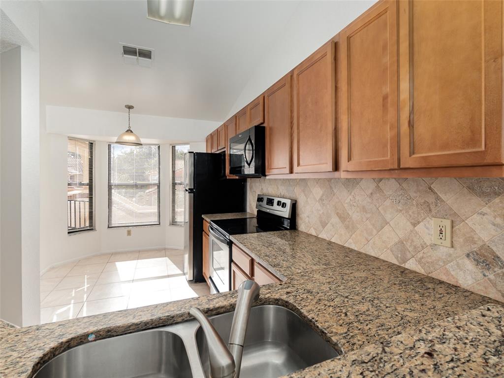 A kitchen features granite countertops, wood cabinets, a stainless steel sink, and a breakfast nook — 7654 SUGAR BEND DR DRIVE UNIT 7654, ORLANDO, FL