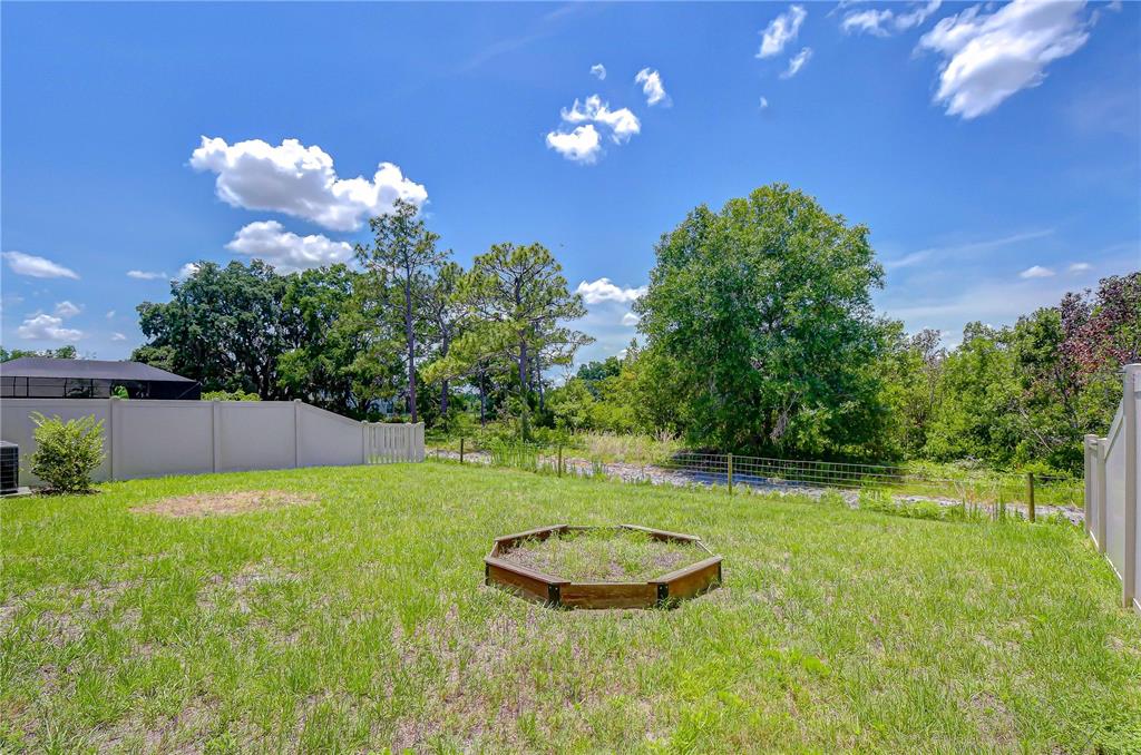 A grassy backyard features a wooden hexagonal planter box and a white vinyl privacy fence — 21534 VIOLET PERIWINKLE DRIVE, LAND O LAKES, FL