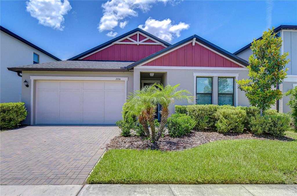 A single-story house with a two-car garage, red gable siding, and a landscaped front yard — 21534 VIOLET PERIWINKLE DRIVE, LAND O LAKES, FL