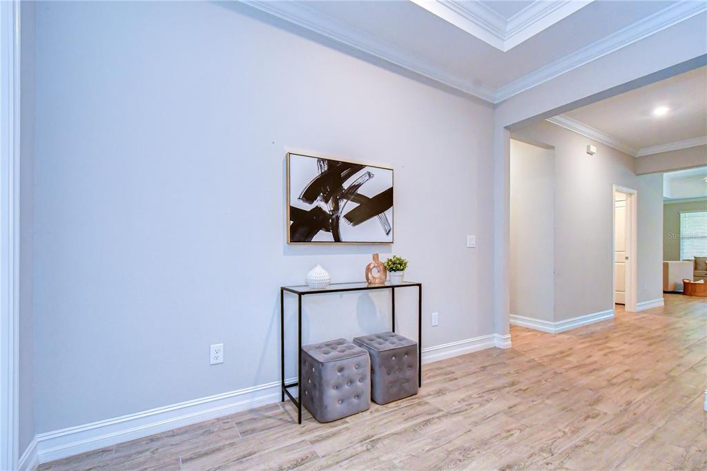A modern entryway features light wood-look tile flooring, a glass console table, and abstract art — 21534 VIOLET PERIWINKLE DRIVE, LAND O LAKES, FL