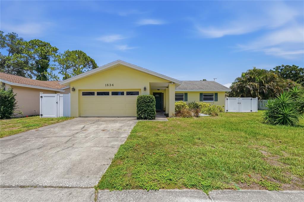 A yellow single-story house with a two-car garage and a concrete driveway — 1634 DALE CIRCLE N, DUNEDIN, FL