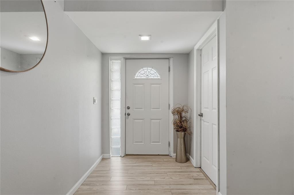 A bright entryway features light wood-look flooring, a white front door, and a glass block window — 1634 DALE CIRCLE N, DUNEDIN, FL