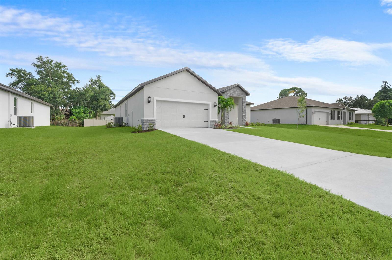 A single-story house with a white exterior, stone accents, and a concrete driveway — 7876 104th Avenue, Vero Beach FL 32967, VERO BEACH, FL