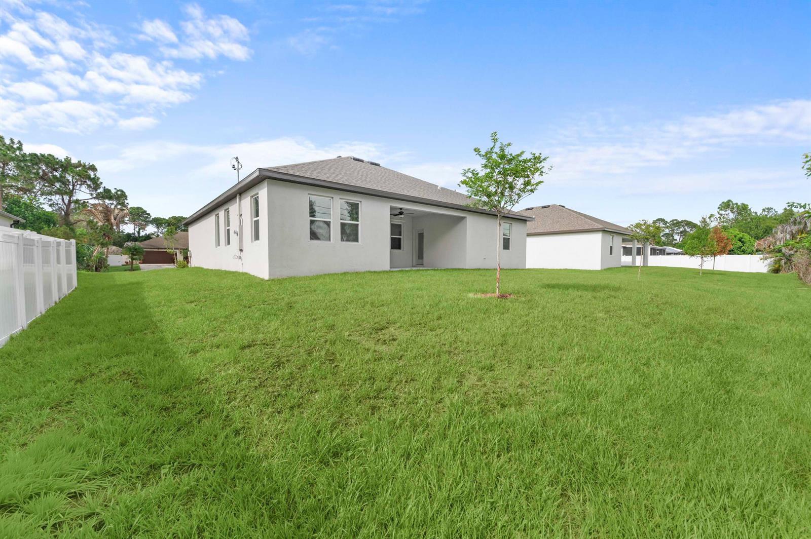 The exterior rear view of a single-story house features a covered patio and lawn — 7876 104th Avenue, Vero Beach FL 32967, VERO BEACH, FL